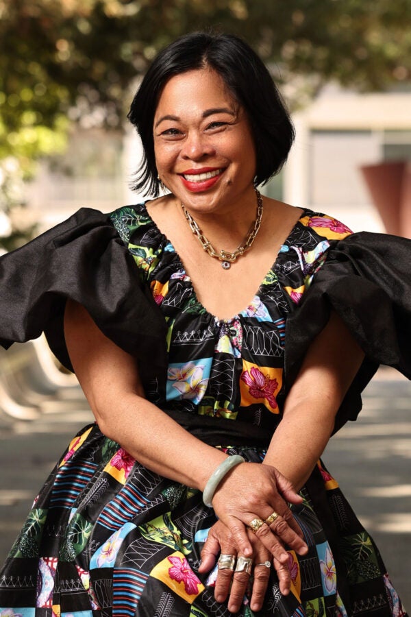 Person sitting in tree lined walkway wearing a colorful dress.