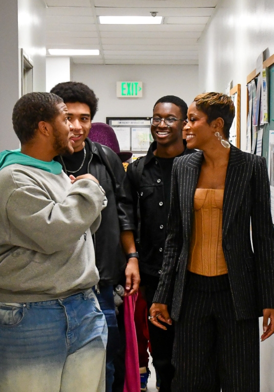 A group of three male students walk down a white hallway with Keke Palmer